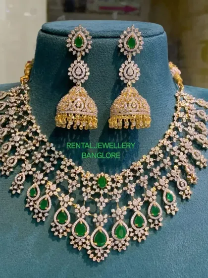 A close-up of a beautiful AD necklace and jhumka set with green stones. The design is intricate and perfect for adding sparkle to your reception outfit.
