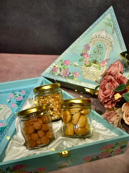 A beautiful triangular gift box for Diwali, containing glass jars filled with my gourmet spiced nuts and cookies. The packaging itself is a keepsake.