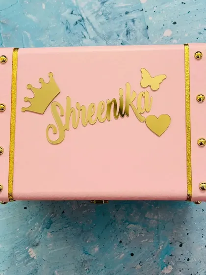 Shown here in a soft pink, this personalized trunk box is a popular choice for gifting. The combination of the name, crown, butterfly, and heart charms creates a truly charming piece.