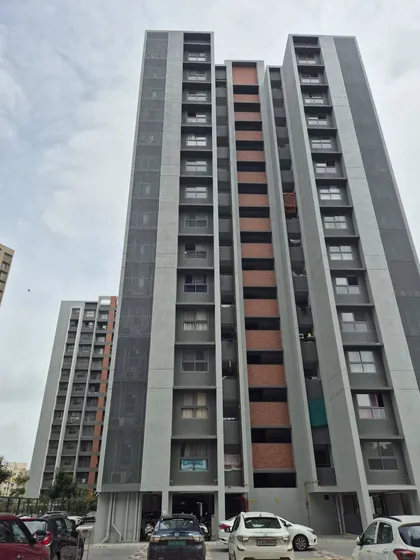 A ground-level view of the completed Adani Amogha towers in Ahmedabad. The facade design incorporates a mix of materials, including textured concrete and brick-colored accents, to create visual interest and texture.