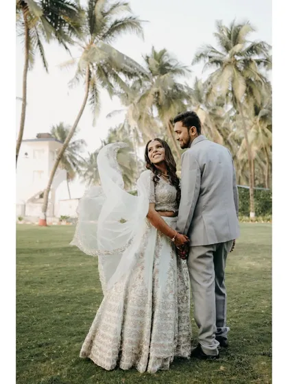 A lovely portrait of the engaged couple in a garden with palm trees. The bride's flowing white lehenga and the couple's happy expressions make this a perfect engagement memory.