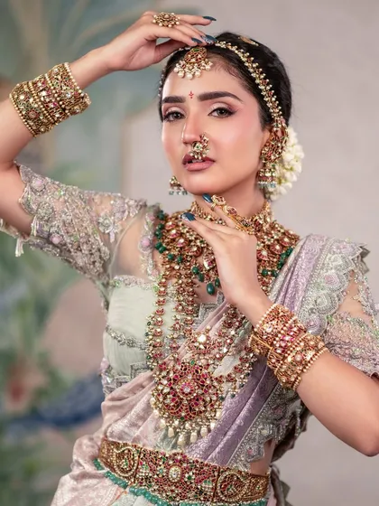 A dynamic pose that captures the grace and movement of the model. The hands are positioned to draw attention to the face and the stunning layered necklaces.