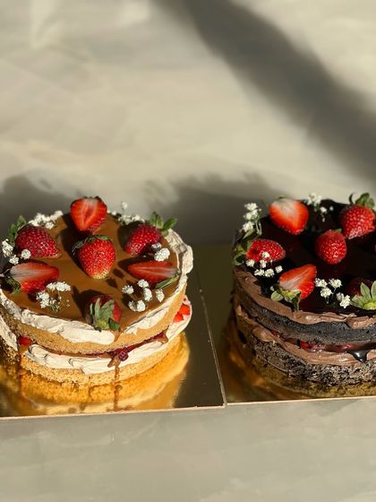 Two of our beautiful strawberry cakes side-by-side. One features a caramel topping, and the other is a rich chocolate version, both loaded with fresh strawberries.