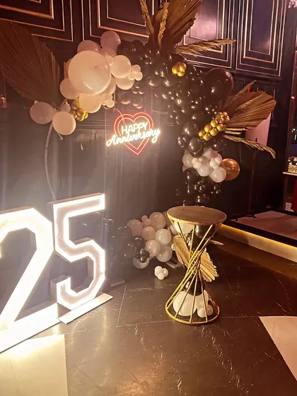 A modern and chic black, white, and gold balloon arrangement for a 25th anniversary party. This style is perfect for evening events and adds a touch of glamour with its marquee numbers and neon sign.
