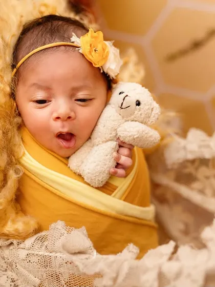 A luxury newborn session featuring a beautiful baby girl in a yellow, sunflower-themed setup. The vibrant color and soft textures make for a cheerful portrait.