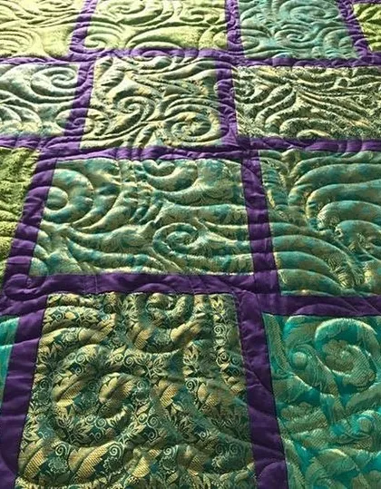 A close-up of a quilt with rich, textured quilting in shades of green and purple.