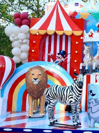 A close-up of the carnival decor, featuring a lion and zebra prop in front of a colorful rainbow and a red and white striped tent.
