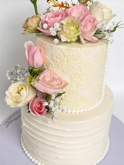 A view of the two-tiered floral wedding cake, showing the different textures on each tier: a subtle pattern on top and rustic lines on the bottom.