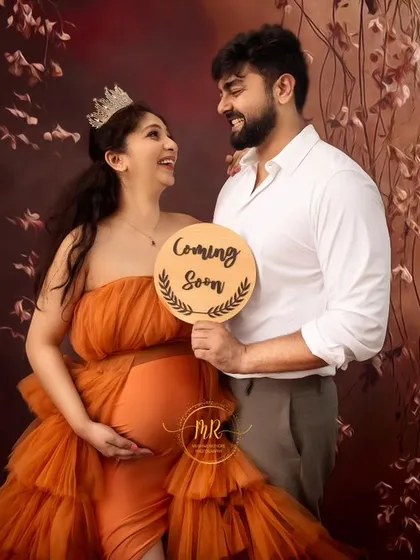 A fun pregnancy announcement photo. The couple smiles at each other while the partner holds a "Coming Soon" sign, adding a playful touch to their maternity shoot.