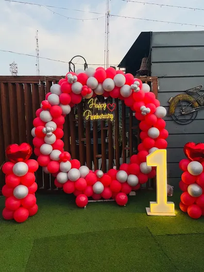 A clear, straight-on view of the red and silver circular balloon backdrop, showcasing the "Happy Anniversary" neon sign and the prominent "1" marquee light.