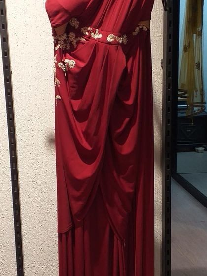 A draped red one-shoulder gown with delicate floral embroidery along the waist. The Grecian-style draping is flattering and timeless, making it a great choice for a formal event.