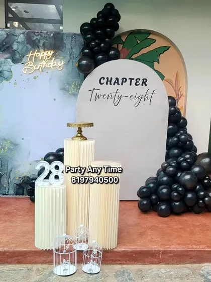 For a more modern and stylish celebration, I offer elegant setups like this 'Chapter 28' birthday. It features a sophisticated black and marble-effect backdrop, a custom arched sign, black chrome balloons, and sleek pedestals for the cake.