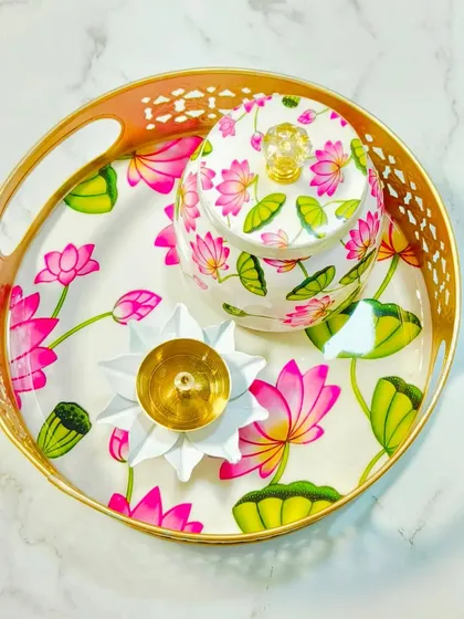 This Pichwai-style set, featuring a tray, a jar, and a brass lotus diya, is perfect for festive gifting and decor. The design is inspired by traditional Indian art, adding an elegant touch to any celebration.