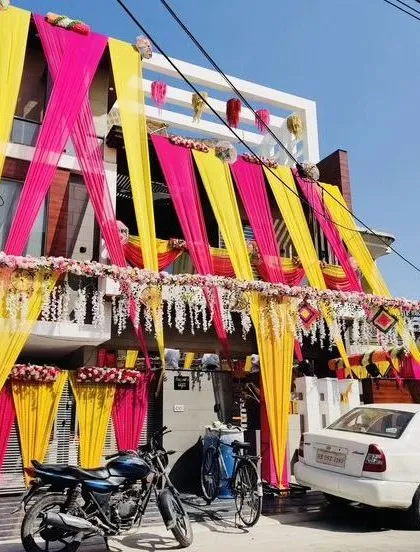A vibrant decoration for a home wedding. The pink and yellow drapes, along with hanging floral strings, create a festive and welcoming atmosphere.