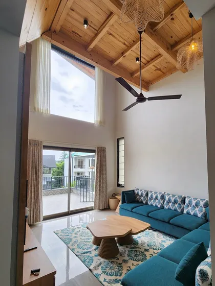 For this beautiful villa in the hills, we designed a living space that feels open and connected to nature. The double height room features a vaulted wooden ceiling, a large teal sectional sofa, and our custom-made wooden coffee table, creating a perfect blend of comfort and rustic charm.