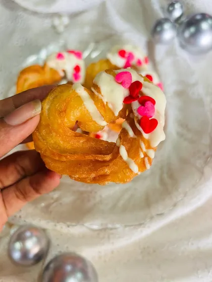 Here is a close-up of my signature heart-shaped churro. You can see the crispy, golden texture of the churro, generously drizzled with creamy white chocolate and topped with red and pink heart-shaped sprinkles for a festive touch.
