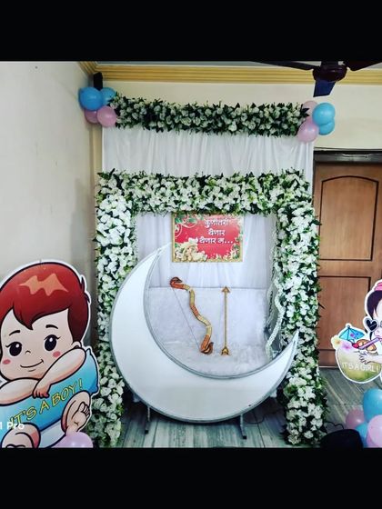 The same home baby shower setup in natural light, showing the white floral arch and the 'Kunitari Yenar Yenar Ga' sign.