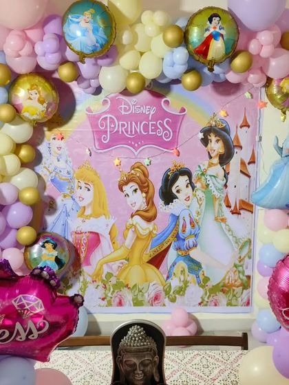 A dreamy Disney Princess party. This setup includes a large backdrop featuring multiple princesses, surrounded by a pastel-colored balloon arch.