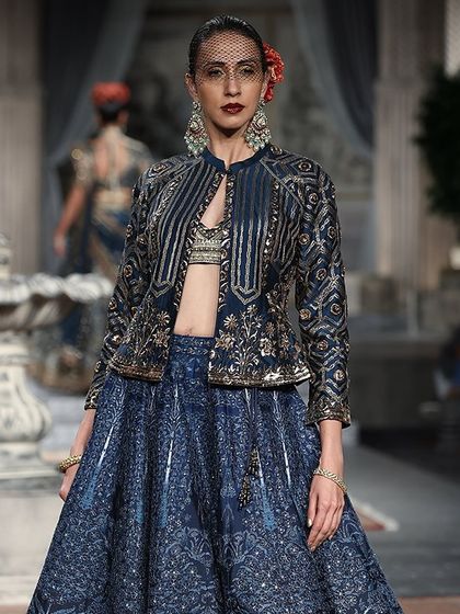 A high-fashion look from the runway. This indigo blue lehenga with a structured, embroidered jacket shows the kind of designer styles that inspire our collection.