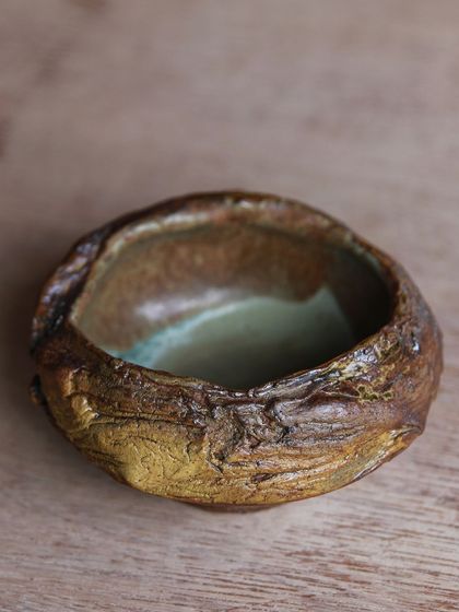 A small, textured bowl with a rich, earthy exterior and a contrasting green interior, a result of playing with foraged materials and glazes.