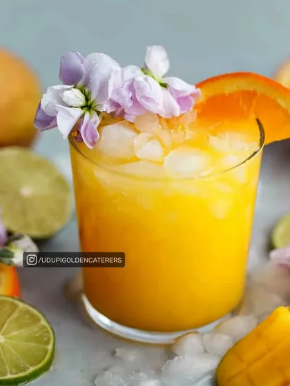 A glass of our refreshing Mango and Orange Delight, garnished with fresh flowers and fruit slices. We offer a wide variety of fresh fruit juices and welcome drinks for your events.