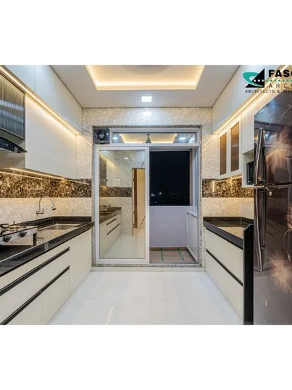 A parallel kitchen in Bhiwandi with a view into the dry balcony. The design uses a mix of dark and light marble-patterned laminates and features a large refrigerator, demonstrating efficient space planning.