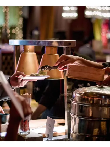 A guest is served steaming hot dumplings at a busy live station. The bokeh background of the event shows how our stations become a hub of activity and enjoyment.