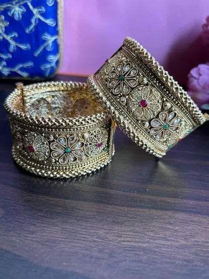 A pair of broad, antique-finish bridal bangles ('kadas') with detailed floral work.