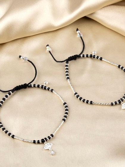 A pair of Nazariya-style anklets or bracelets with black beads and a silver diamond-shaped charm.