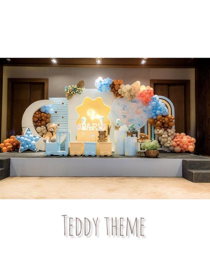 A wide shot of a 'Teddy Theme' party stage, with a large 'Happy Birthday' sign, character props, and a beautiful blue and brown color scheme.