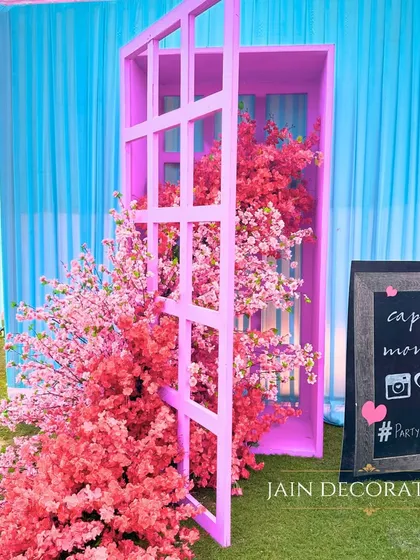 A whimsical photo booth with a pink door opening to a cascade of cherry blossoms. The "capture the moment" sign encourages guests to have fun and make memories.