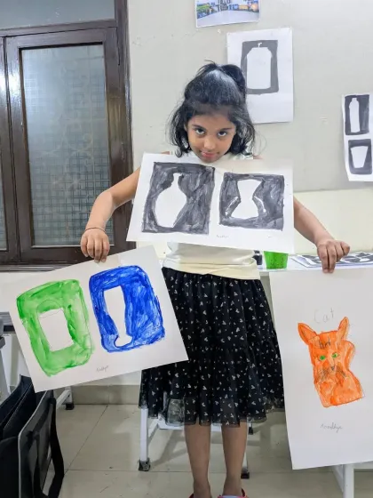 This student proudly displays her work on positive and negative space, along with a colorful cat painting. These exercises are key to understanding composition.