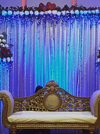 This stage rental uses cool-toned blue lighting to create a sophisticated atmosphere. The decor includes a traditional golden sofa, a curtain backdrop with crystal strings, and two large floral arrangements on pillars.