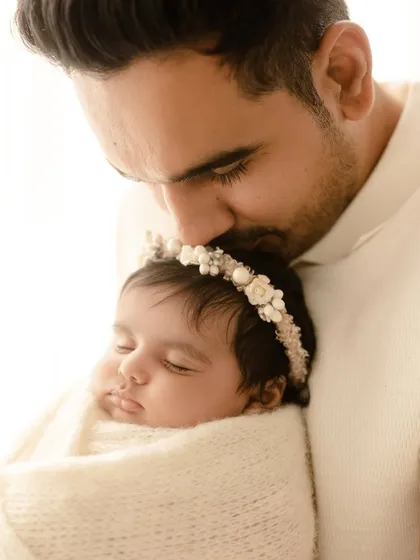 A delicate close-up of a father kissing his newborn daughter's forehead. The baby's floral headband adds a sweet, gentle touch to this loving portrait.