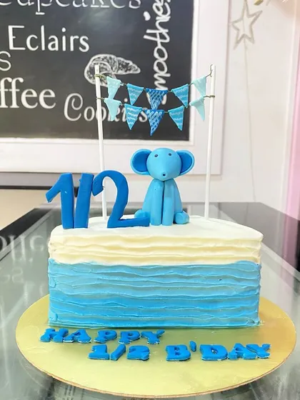 A simple and sweet half-birthday cake in shades of blue. The design features a small elephant topper and a banner.