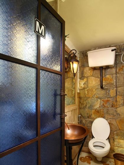 Even the restroom at Amour Bistro reflects the restaurant's rustic, industrial-chic aesthetic. A stone wall, copper sink, and frosted glass door with a vintage-style lantern create a cohesive design experience.