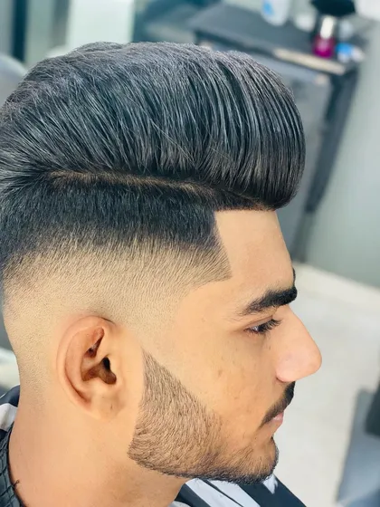 A perfect example of a high-volume pompadour with a skin fade that blends seamlessly into the beard. Every line is clean, sharp, and intentional, creating a powerful, modern look.