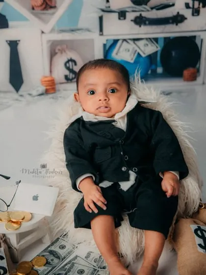This little boss is awake and ready for business. The full setup with money bags and a tiny laptop completes the scene.