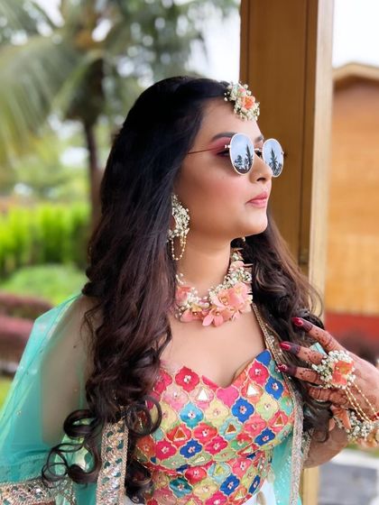 A fun, candid shot of the Haldi bride. Her colorful makeup, floral jewellery, and cool sunglasses perfectly capture the happy and relaxed vibe of the ceremony.