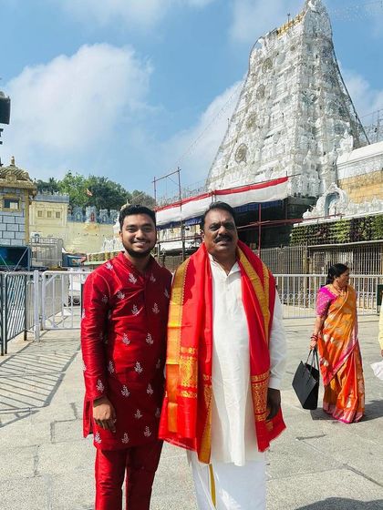 A father and son duo in our custom ethnic wear for a temple visit. The son wears a vibrant red kurta set with detailed embroidery, showcasing our versatility for different occasions.
