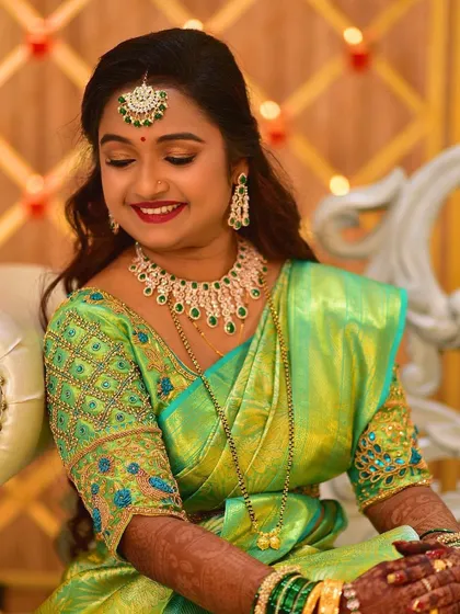 A shy, smiling bride ready for her reception. Her look features a shimmering green saree, diamond jewelry, and a soft, glamorous makeup look.