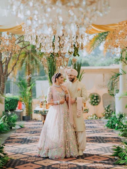 A stunning portrait of the couple under a canopy of chandeliers and lush greenery. This shot combines opulent decor with a genuine, happy moment.