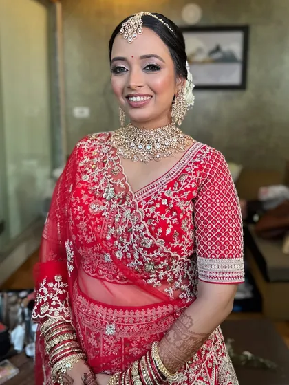 A smiling bride in her red wedding lehenga, her hair styled in a classic white floral bun.