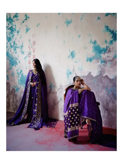 Two models showcase the versatility of our purple sarees. One is a classic drape, while the other features a heavily embroidered shawl, demonstrating different ways to style these heritage pieces.