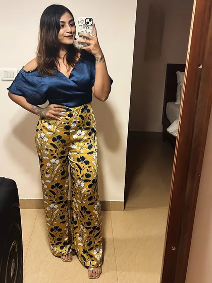 A mirror selfie showing a bold and stylish outfit. I've paired a navy off-the-shoulder top with vibrant yellow floral-print satin pants.