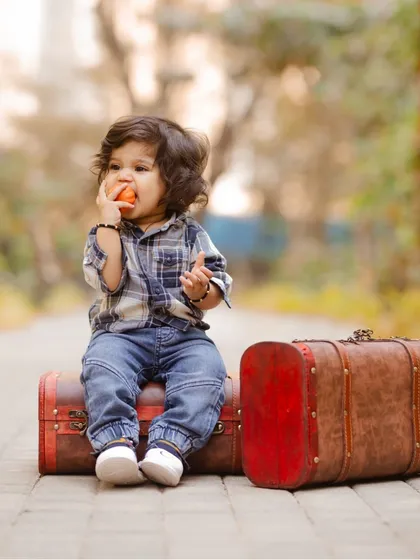 A 'little traveler' theme for a baby shoot, with the child sitting on vintage suitcases on a pathway.