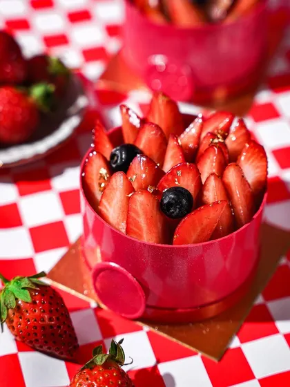 An individual strawberry mousse cake on a red and white checkered background. The strong shadows and bright colors give this shot a fun, graphic, and modern diner vibe.