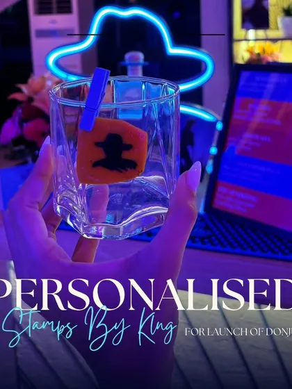 A guest holding a glass with our custom Don Julio stamped garnish, perfectly framed by the event's neon sign.
