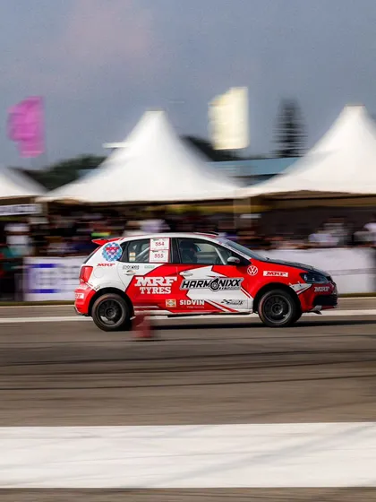 A Volkswagen Polo rally car, sponsored by MRF Tyres, in a dynamic panning shot. The motion blur effectively conveys the high speed of the race.