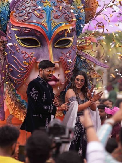 Chasing thrills and making memories. A couple makes a grand entrance at their carnival-themed party on a massive, ornate float with a Venetian mask.